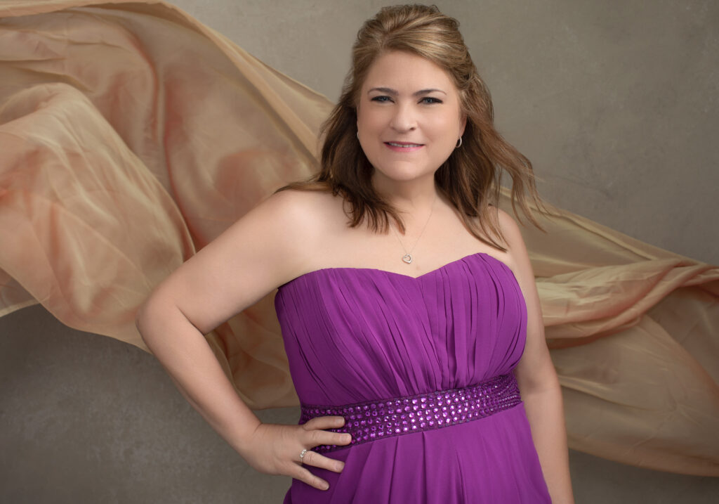 A vibrant personal branding portrait of a Cincinnati woman in a strapless purple gown with sparkling details at the waist. A soft, flowing peach-colored fabric cascades in the background, adding elegance and movement. This empowering image is ideal for women in the Cincinnati area looking for glamorous and sophisticated portraits.