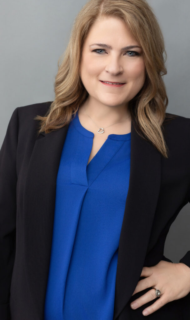  A close-up Cincinnati professional headshot of a woman in a black blazer and royal blue blouse against a neutral gray background. Her confident expression and polished appearance make this portrait ideal for executives and professionals in the Cincinnati area seeking standout branding imagery.