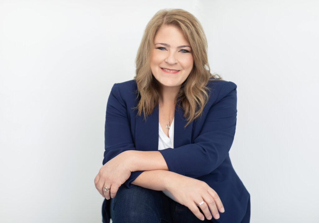 A relaxed Cincinnati headshot of a professional woman seated against a clean, white background. Wearing a navy blazer, white top, and jeans, she leans forward with a friendly and approachable smile. This personal branding portrait is tailored for professionals and entrepreneurs in Cincinnati.