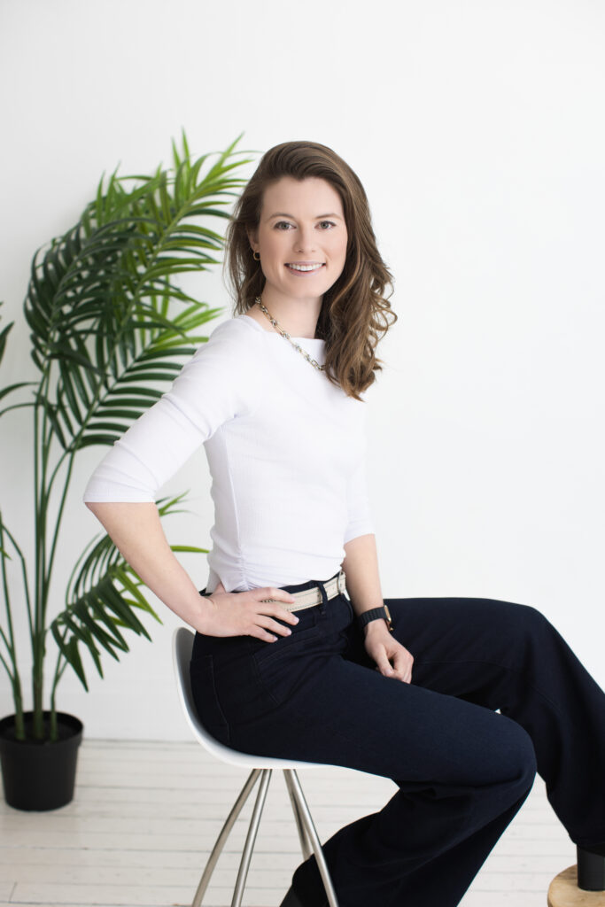 Bright and approachable portrait of a woman in a white top and wide-leg pants, seated with a natural plant backdrop. Janel Lee Photography in Cincinnati provides fresh, authentic headshots perfect for LinkedIn and professional branding.