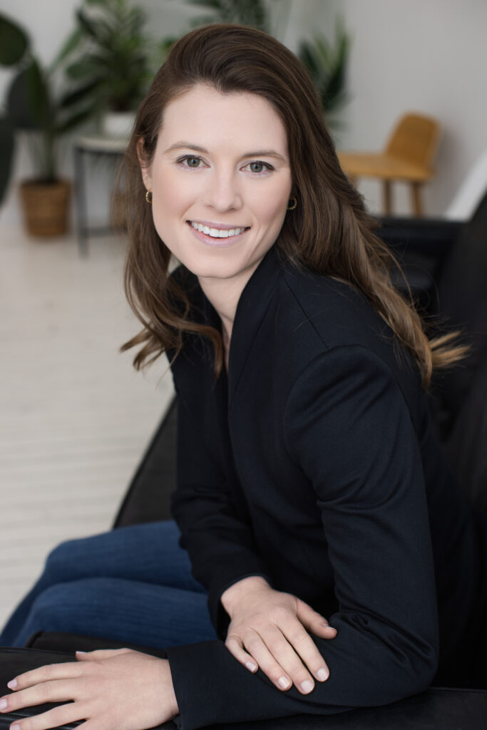 Professional headshot of a woman in a black blazer, seated in a modern office-inspired setting with greenery. Captured by Janel Lee Photography in Cincinnati, Ohio – experts in personal branding photography for entrepreneurs and executives.