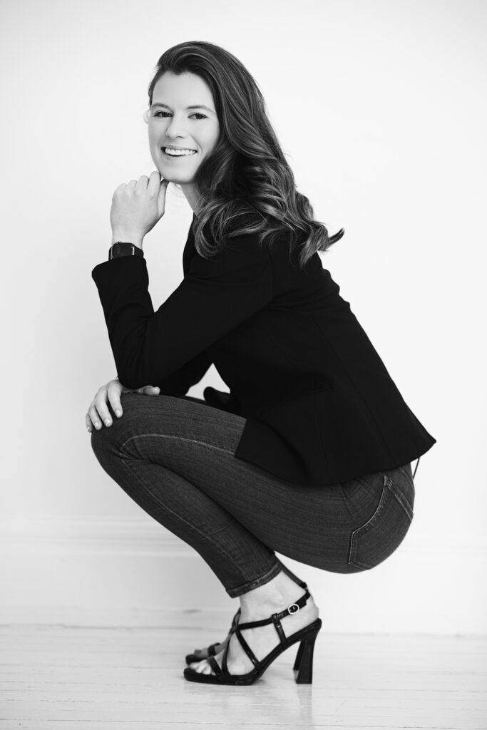 Black-and-white portrait of a smiling woman in a black blazer and jeans against a clean white background. Janel Lee Photography in Cincinnati, Ohio, offers timeless, polished headshots for professionals and entrepreneurs.