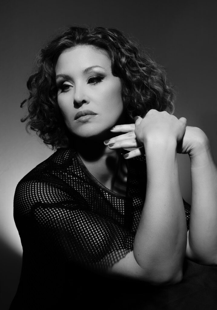 A black-and-white dramatic Cincinnati portrait of a woman resting her chin on her hands, wearing a geometric-patterned top. Captured in a downtown Cincinnati photography studio, this image uses soft directional lighting to create depth and emotion, ideal for personal branding or editorial projects.