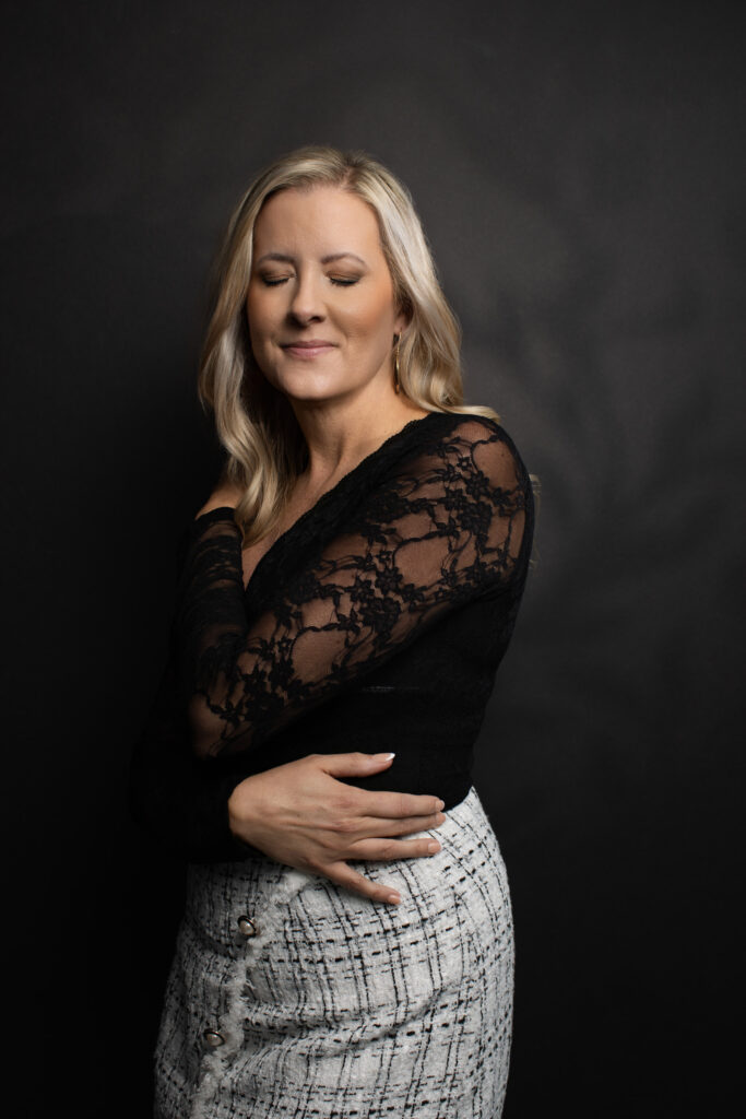 Katie Stuart with eyes closed, wearing lace top and tweed skirt against black backdrop