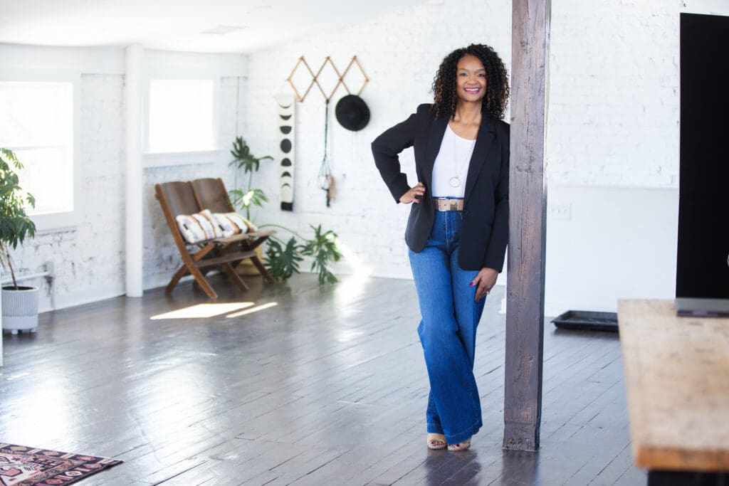 Sheila Eason standing confidently in bright studio space wearing jeans and blazer