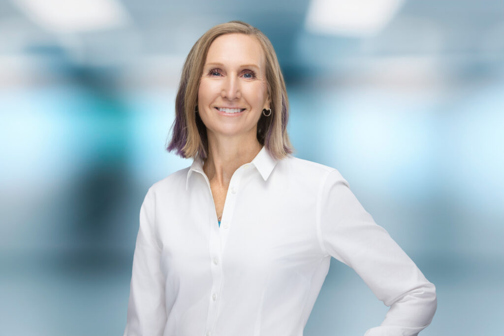 Bright professional headshot of Susan Colby in white shirt with blue background