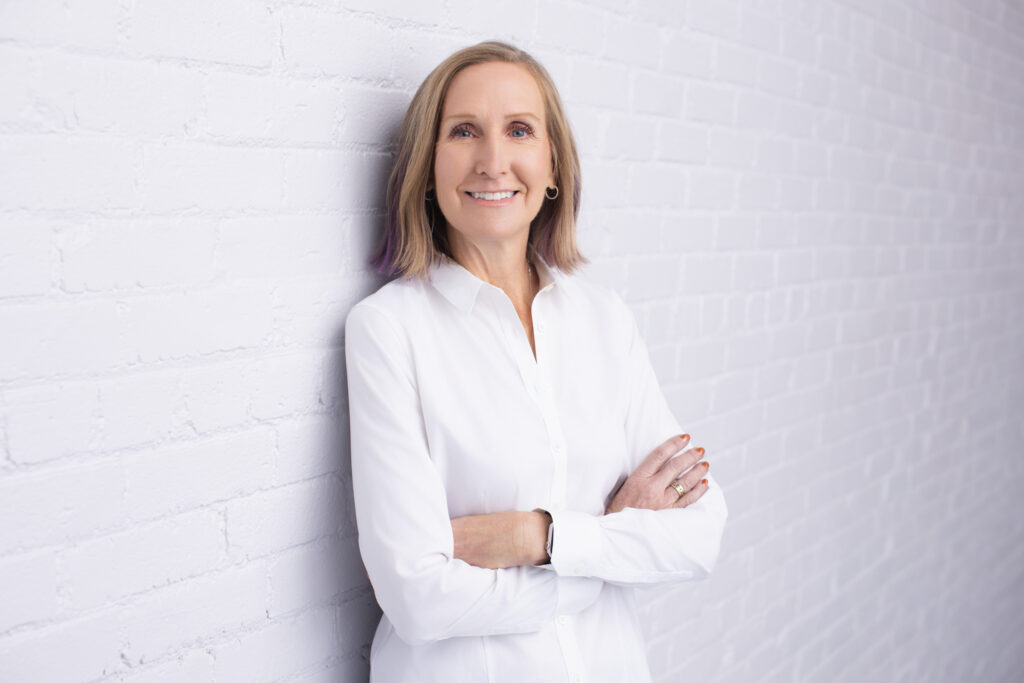 Susan Colby professional headshot leaning against white brick wall in Cincinnati studio