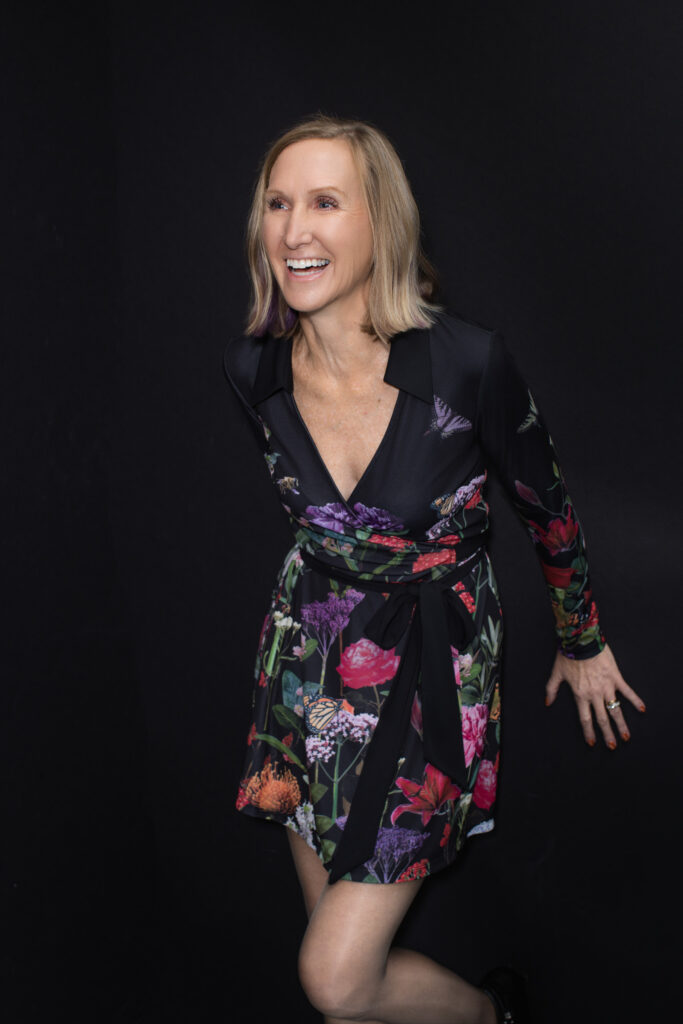 Bold studio portrait of Susan Colby wearing floral dress against black backdrop
