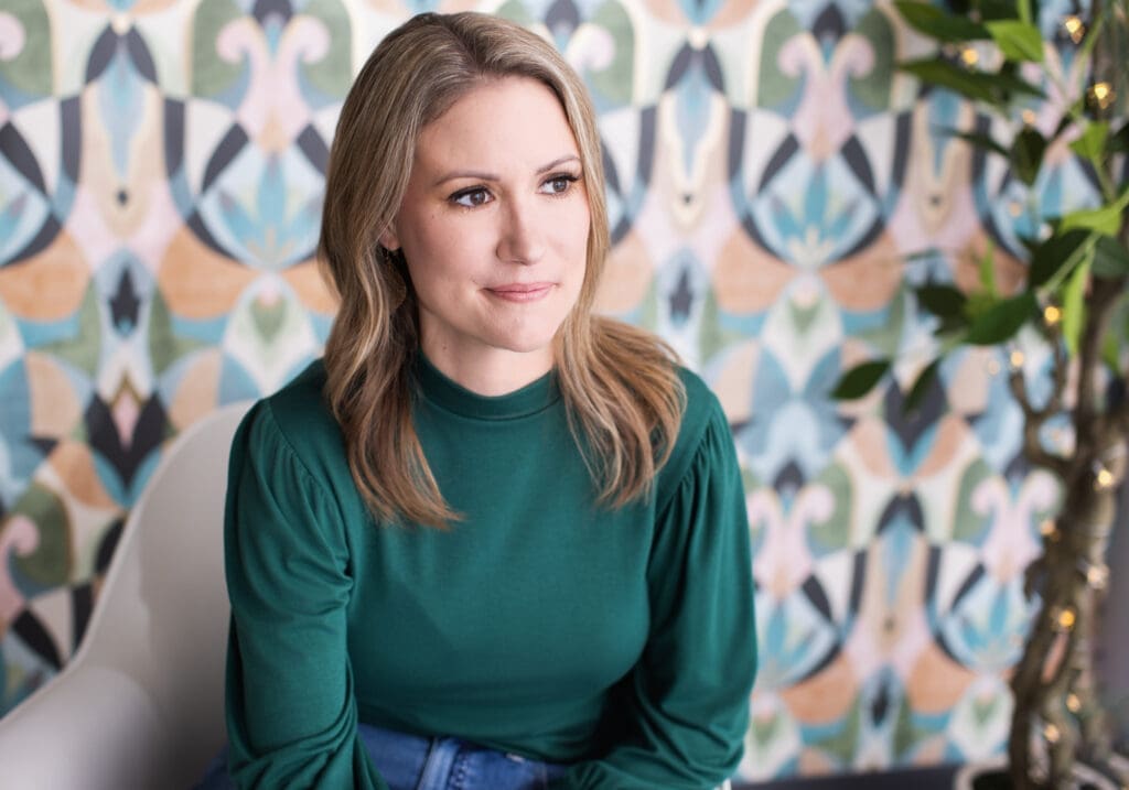 Professional personal branding portrait of a woman in Cincinnati, Ohio wearing a green blouse and seated indoors against a colorful modern backdrop.