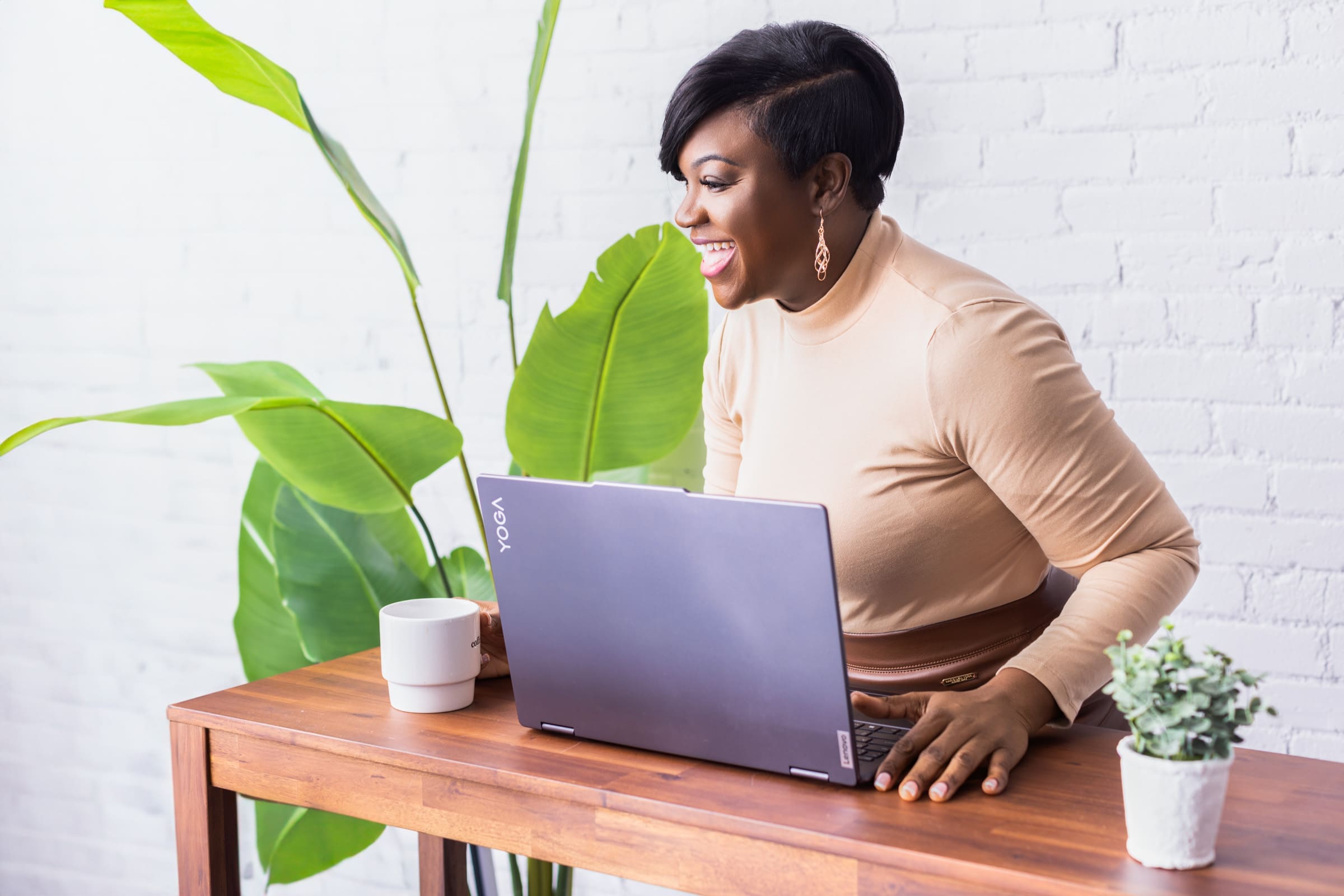 Personal branding photo of writer and speaker Paulette Jones in Cincinnati, Ohio, smiling while working on a laptop at a modern workspace with greenery and a bright studio setting.