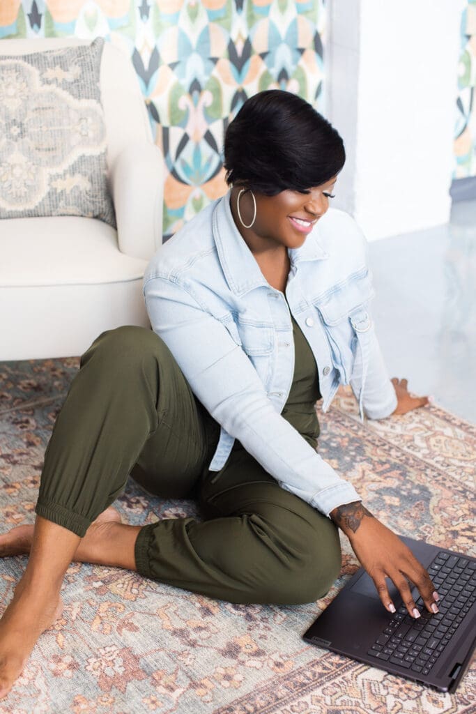 Lifestyle personal branding portrait of writer and speaker Paulette Jones in Cincinnati, Ohio, smiling while working on a laptop seated on a patterned rug in a relaxed studio setting.