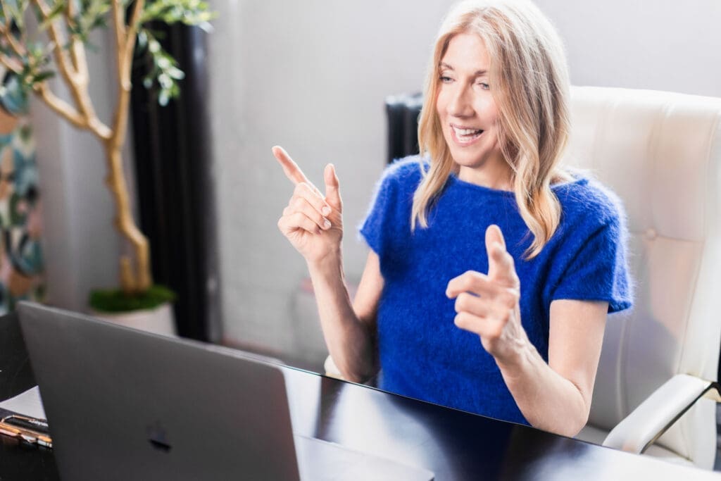 Shelly Wight sits at a laptop in a blue sweater during a Cincinnati Ohio personal branding session styled to represent virtual coaching and leadership development.